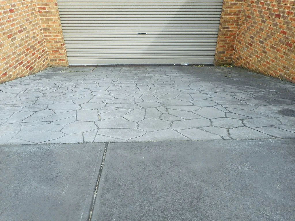 Stamped concrete driveway leading to a garage between brick walls