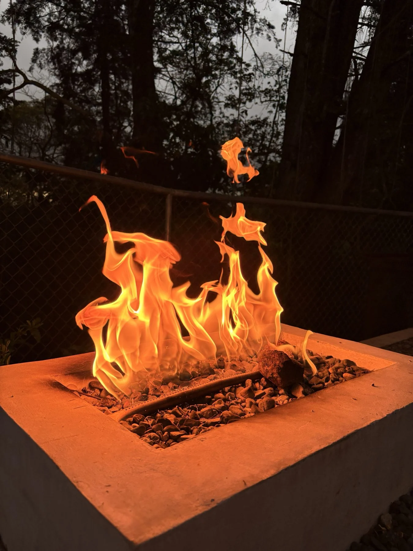 Fire burning in a square concrete fire pit at dusk